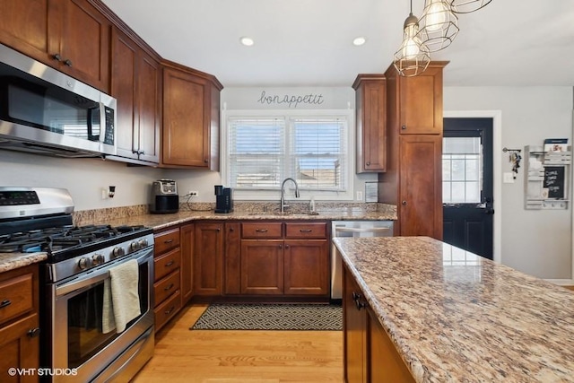 kitchen featuring stainless steel appliances, hanging light fixtures, light hardwood / wood-style flooring, light stone counters, and sink