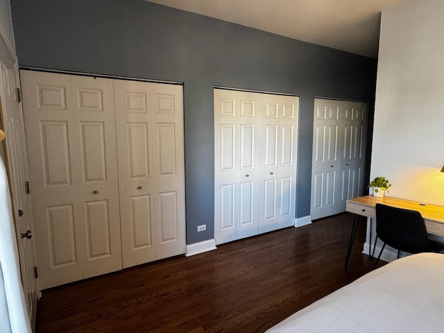 bedroom with dark wood-style floors, baseboards, and two closets