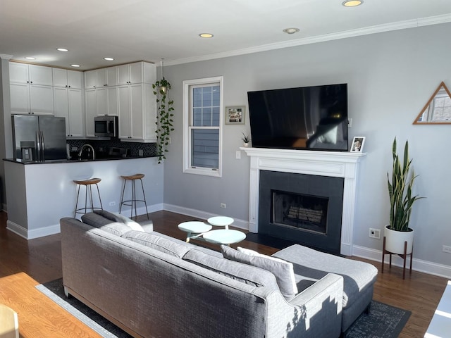 living area with recessed lighting, a fireplace with flush hearth, baseboards, ornamental molding, and dark wood finished floors