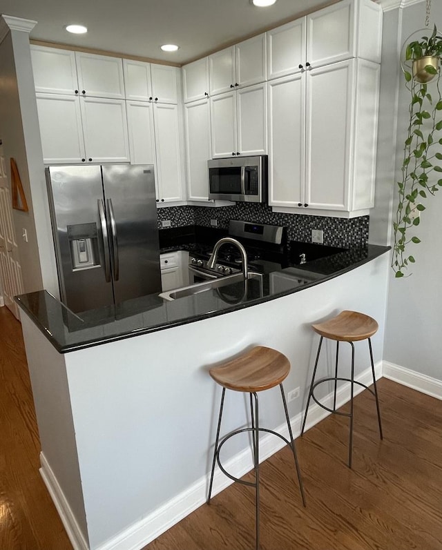 kitchen featuring a peninsula, white cabinetry, appliances with stainless steel finishes, and dark wood-type flooring