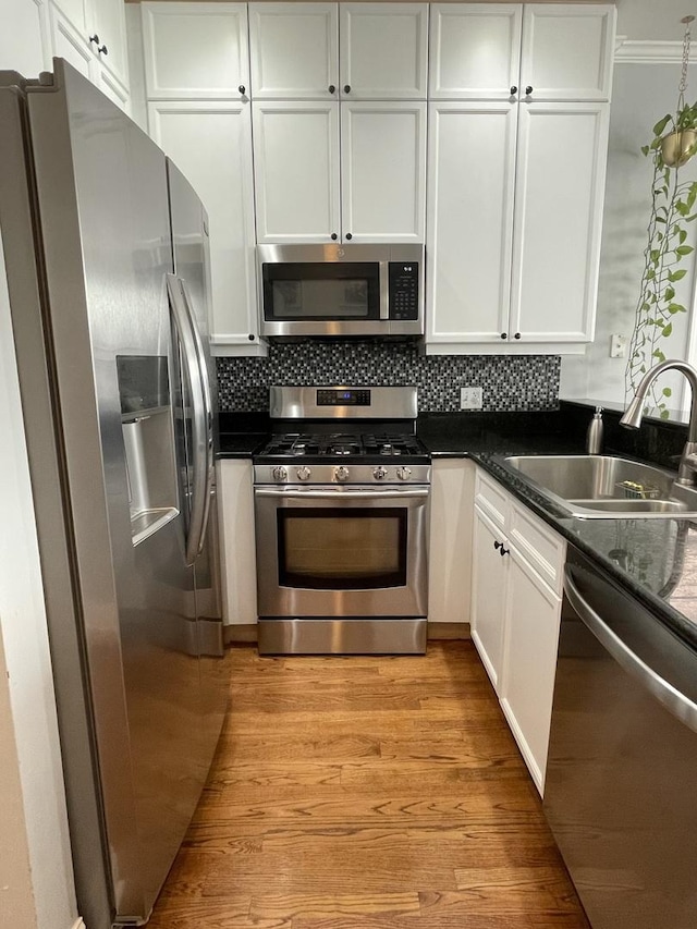 kitchen with a sink, white cabinets, appliances with stainless steel finishes, light wood-type flooring, and decorative backsplash