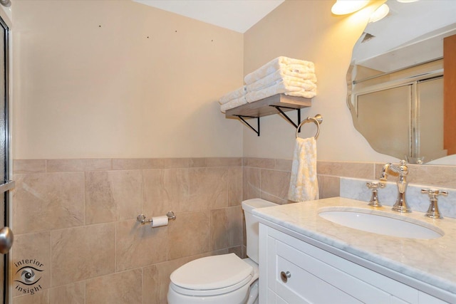 bathroom featuring toilet, vanity, tile walls, and a shower with shower door