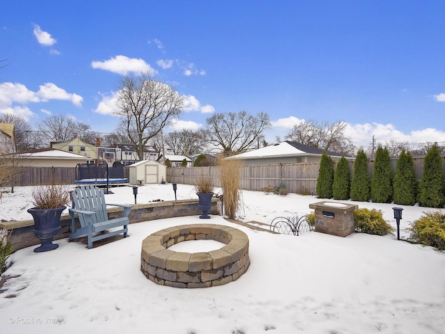 snow covered patio featuring a shed, an outdoor fire pit, and a trampoline