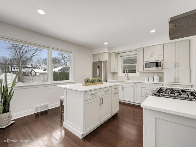 kitchen featuring appliances with stainless steel finishes, a kitchen island, decorative backsplash, sink, and dark hardwood / wood-style floors