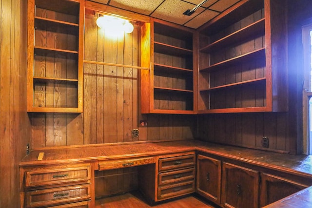 unfurnished office featuring hardwood / wood-style floors, a paneled ceiling, wood walls, and built in desk