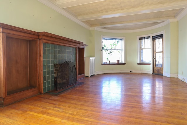 unfurnished living room with a tiled fireplace, hardwood / wood-style flooring, ornamental molding, and beamed ceiling