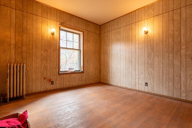 spare room featuring light wood-type flooring, wood walls, and radiator