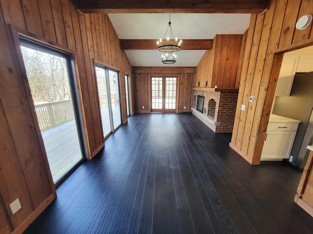 unfurnished living room with wood walls, a brick fireplace, dark hardwood / wood-style floors, a notable chandelier, and beam ceiling