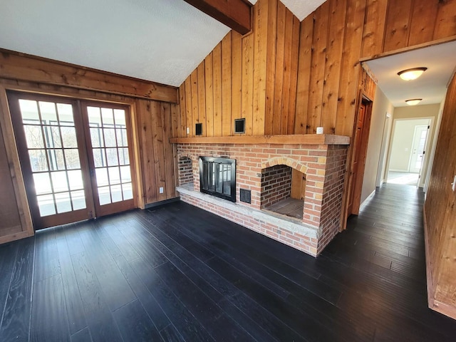 unfurnished living room featuring vaulted ceiling with beams, a brick fireplace, wooden walls, and dark hardwood / wood-style floors