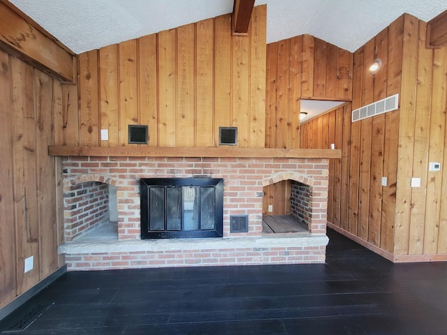 unfurnished living room featuring a textured ceiling, wooden walls, dark hardwood / wood-style floors, lofted ceiling with beams, and a brick fireplace