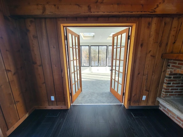 hall featuring a skylight, dark hardwood / wood-style flooring, french doors, and wooden walls