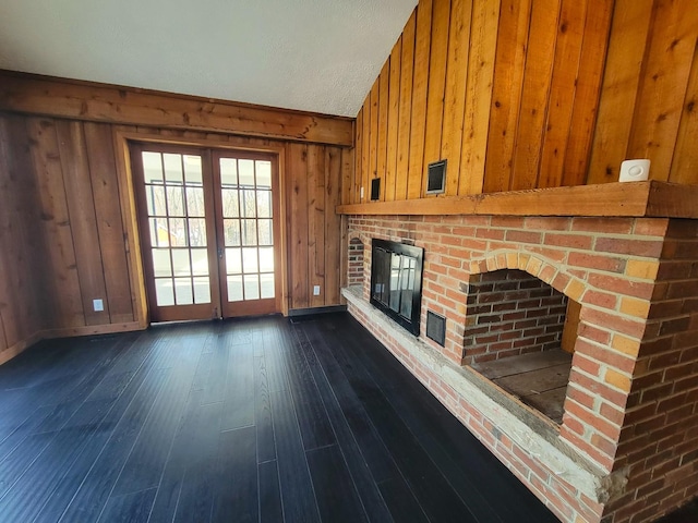 unfurnished living room with french doors, a brick fireplace, dark hardwood / wood-style flooring, and wood walls