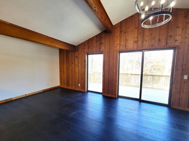 unfurnished room with a notable chandelier, dark hardwood / wood-style floors, wood walls, lofted ceiling with beams, and a textured ceiling