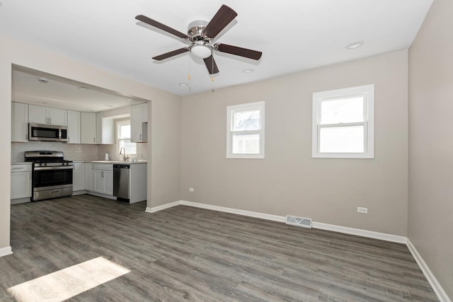 kitchen with ceiling fan, hardwood / wood-style floors, decorative backsplash, white cabinetry, and appliances with stainless steel finishes