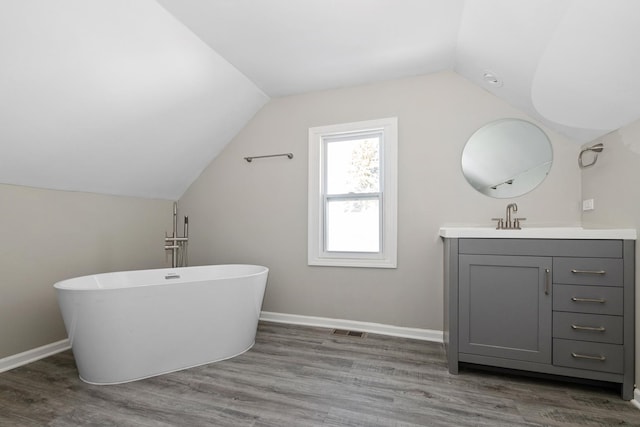 bathroom with vaulted ceiling, a tub to relax in, hardwood / wood-style floors, and vanity