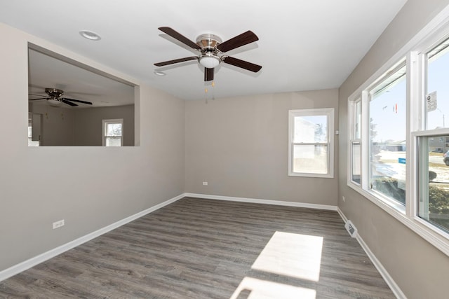 empty room with dark wood-type flooring, plenty of natural light, and ceiling fan