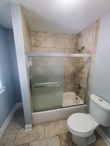 bathroom with toilet, shower / bath combination with glass door, and a textured ceiling