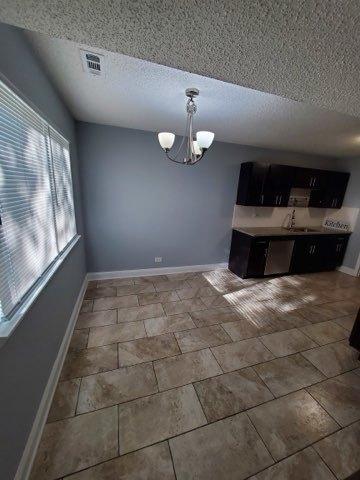 unfurnished dining area featuring a textured ceiling, sink, and a notable chandelier