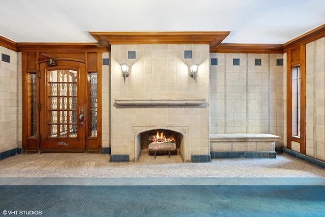 interior space with carpet, ornamental molding, tile walls, and a lit fireplace