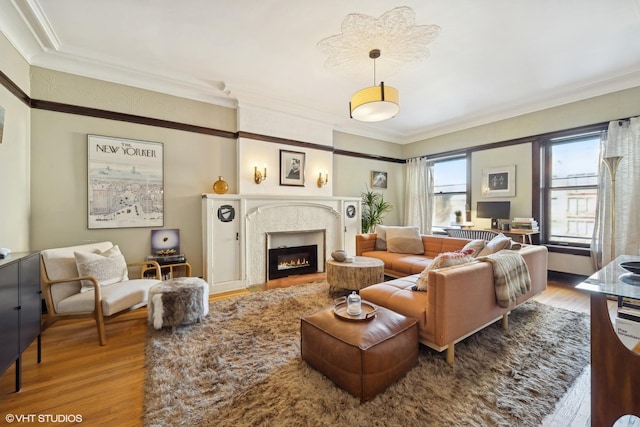 living area featuring a warm lit fireplace, wood finished floors, and crown molding