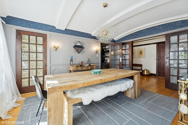 dining space featuring vaulted ceiling with beams, a chandelier, wood finished floors, and french doors