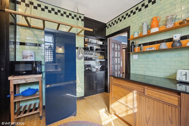 kitchen featuring light wood-style flooring, black appliances, decorative backsplash, open shelves, and dark countertops