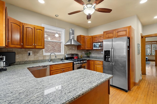 kitchen featuring wall chimney exhaust hood, sink, hanging light fixtures, kitchen peninsula, and stainless steel appliances