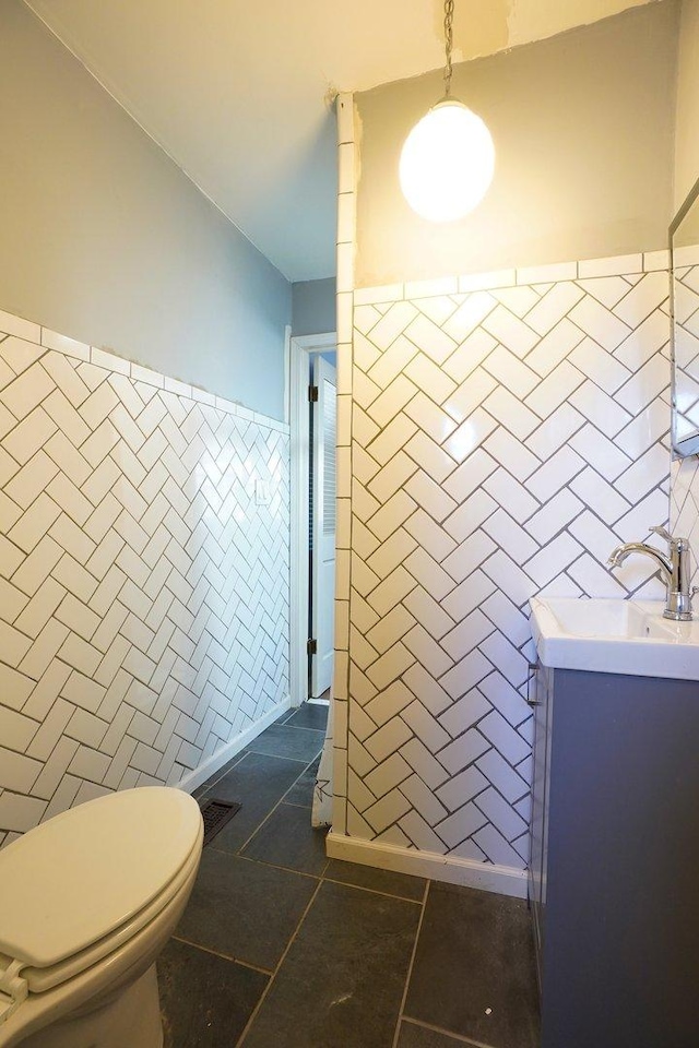 bathroom with toilet, tile patterned flooring, tile walls, and vanity