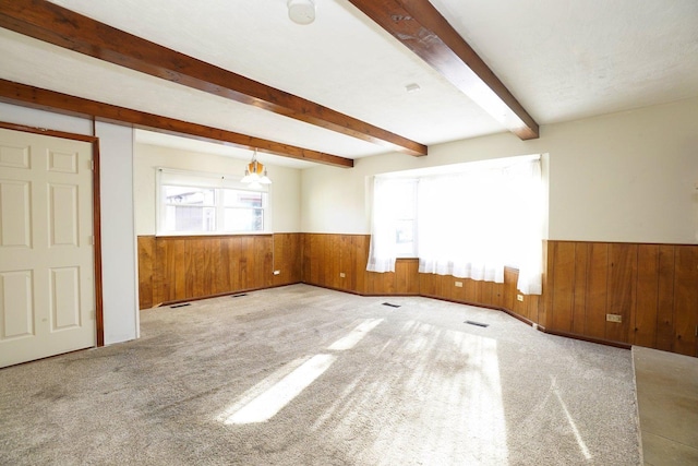 unfurnished room featuring beam ceiling, light colored carpet, and wooden walls