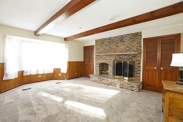 unfurnished living room with a brick fireplace, beam ceiling, light carpet, and wood walls