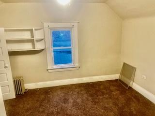 additional living space with dark colored carpet, vaulted ceiling, and radiator