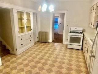 kitchen featuring white cabinetry, radiator, white range with gas cooktop, and decorative light fixtures