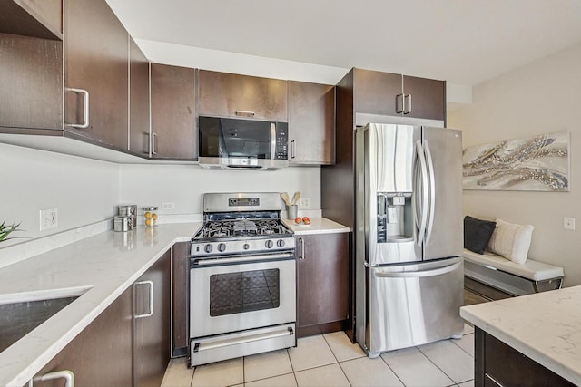 kitchen featuring light tile patterned flooring, dark brown cabinetry, stainless steel appliances, and light stone countertops