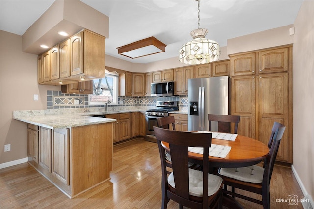 kitchen with appliances with stainless steel finishes, decorative light fixtures, light hardwood / wood-style floors, sink, and backsplash