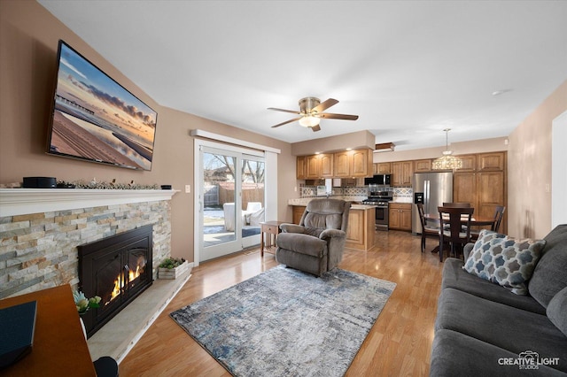 living room featuring a fireplace, ceiling fan, and light wood-type flooring