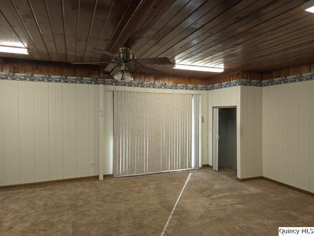 basement featuring carpet, wooden ceiling, ceiling fan, and wood walls