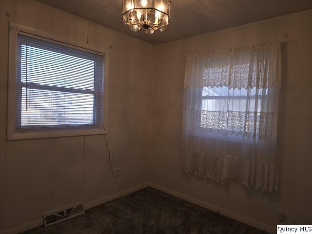 carpeted empty room featuring an inviting chandelier