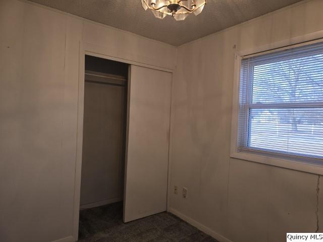 unfurnished bedroom with a notable chandelier, a closet, a textured ceiling, and dark colored carpet