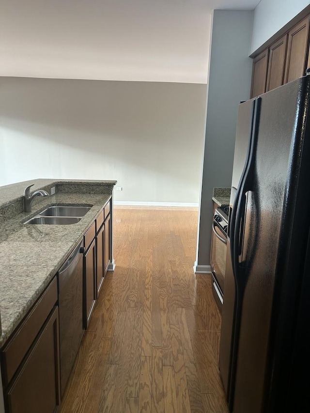 kitchen with black fridge with ice dispenser, dishwasher, sink, light stone countertops, and hardwood / wood-style floors