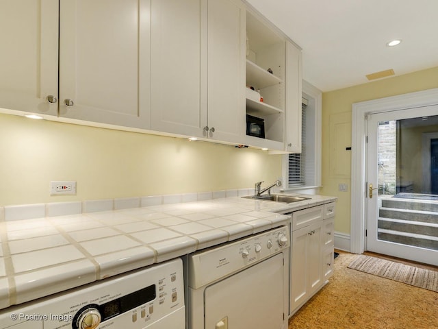 kitchen featuring tile countertops, white dishwasher, white cabinets, washer / clothes dryer, and sink