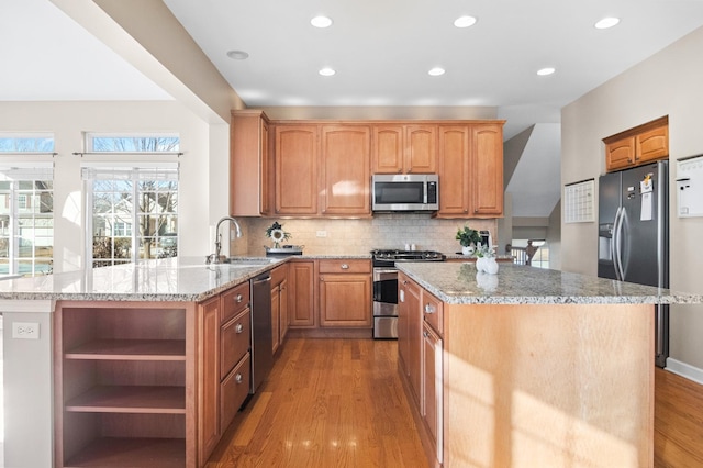 kitchen featuring stainless steel appliances, light stone countertops, sink, and kitchen peninsula