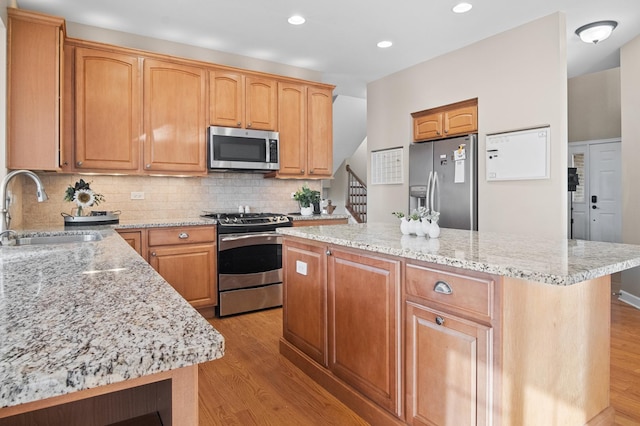 kitchen with sink, appliances with stainless steel finishes, a center island, light stone counters, and light hardwood / wood-style floors