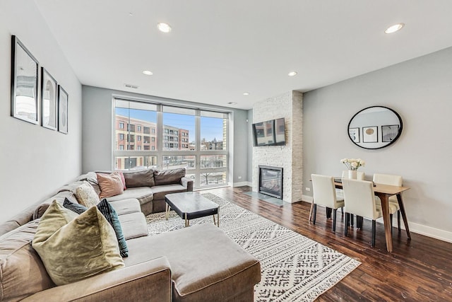 living room featuring a stone fireplace and dark wood-type flooring