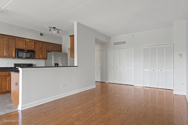 kitchen featuring a textured ceiling, stainless steel fridge, stove, and light wood-type flooring