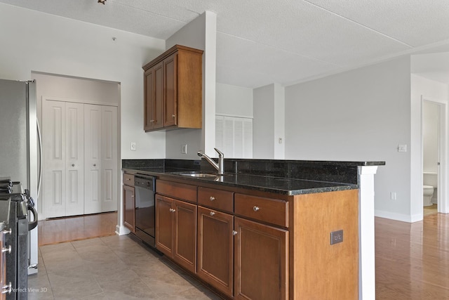 kitchen featuring gas stove, black dishwasher, dark stone countertops, sink, and stainless steel refrigerator