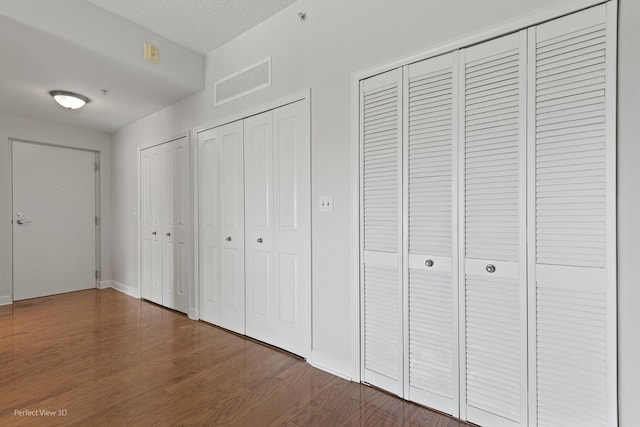 unfurnished bedroom featuring a textured ceiling, dark wood-type flooring, and two closets