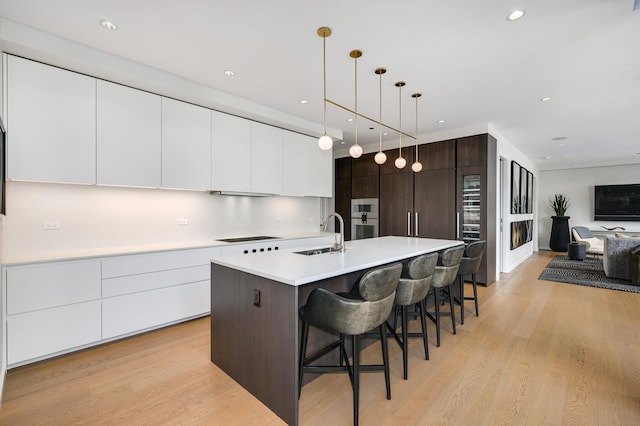 kitchen with sink, hanging light fixtures, dark brown cabinets, light hardwood / wood-style flooring, and an island with sink