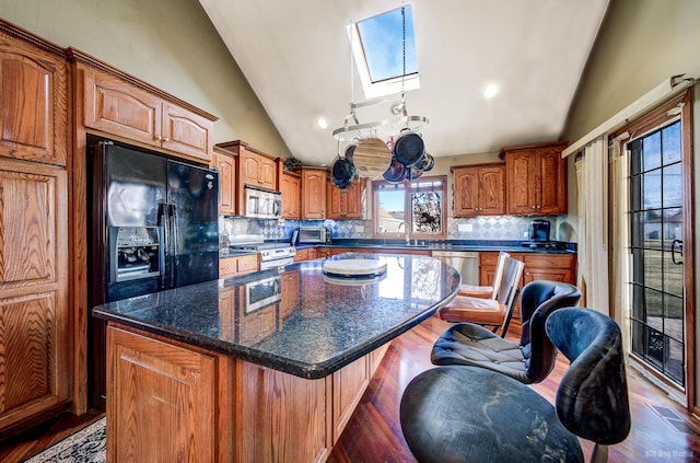 kitchen featuring tasteful backsplash, dark hardwood / wood-style floors, a kitchen island, stainless steel appliances, and vaulted ceiling with skylight