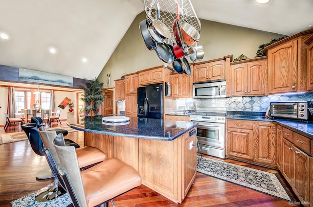 kitchen with wood-type flooring, a center island, high vaulted ceiling, appliances with stainless steel finishes, and decorative backsplash