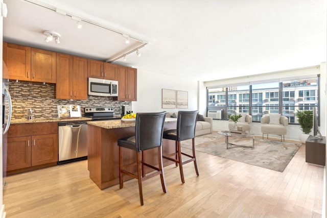 kitchen with a kitchen island, stainless steel appliances, light hardwood / wood-style floors, light stone counters, and a breakfast bar